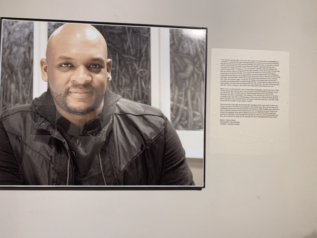 Portrait of Clayton Shelvin smiling beside his story on the wall at the exhibit.