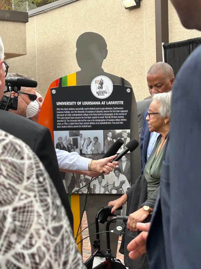 A reporter holds a microphone in front of Joyce Constantine Henson, sister of one of the first African American students to attend UL Lafayette (then SLI).